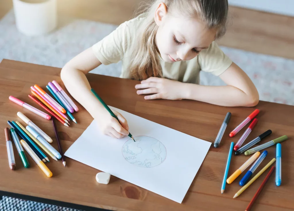 A little girl is drawing at a table with colored pencils.
