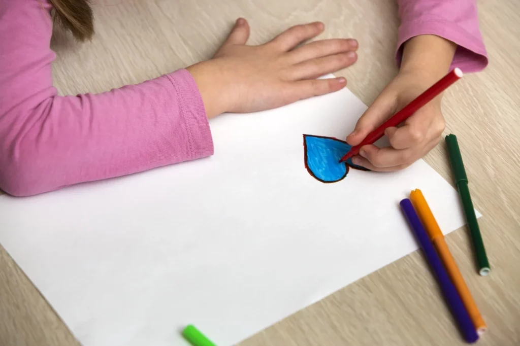 A child is drawing a raindrop on a piece of paper.
