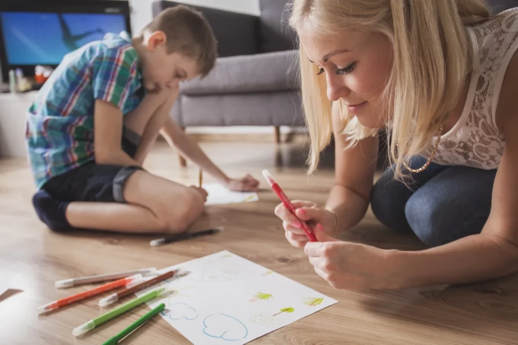 A woman and her son are drawing on the floor.