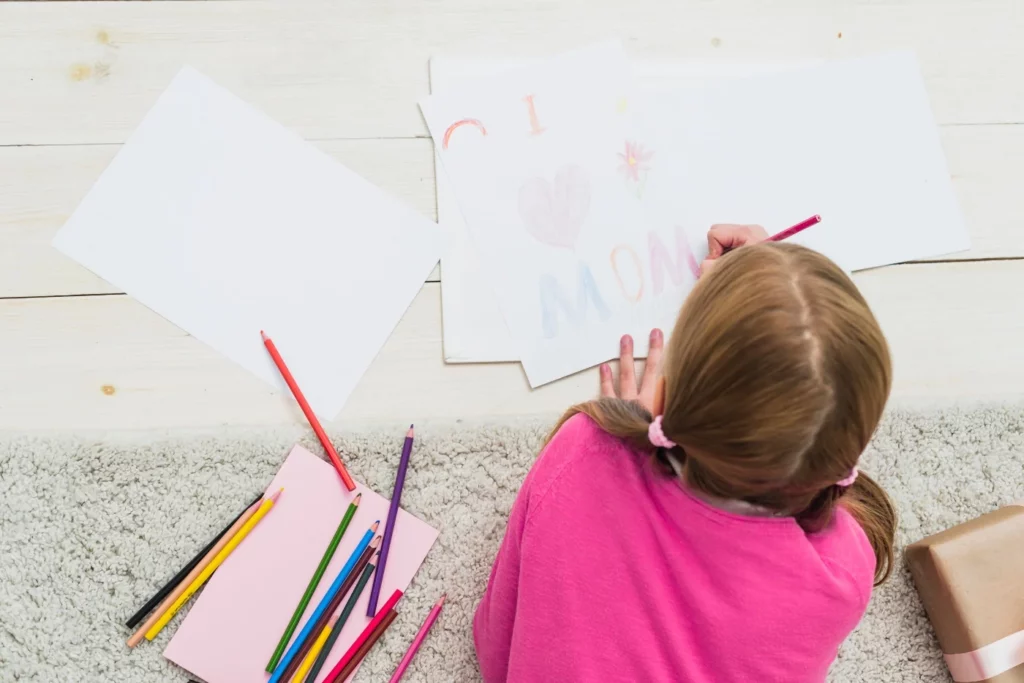 A little girl is drawing on the floor with colored pencils.